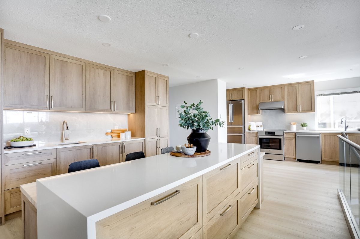 Renovated kitchen with light oak cabinetry, a long white quartz island and stainless appliances